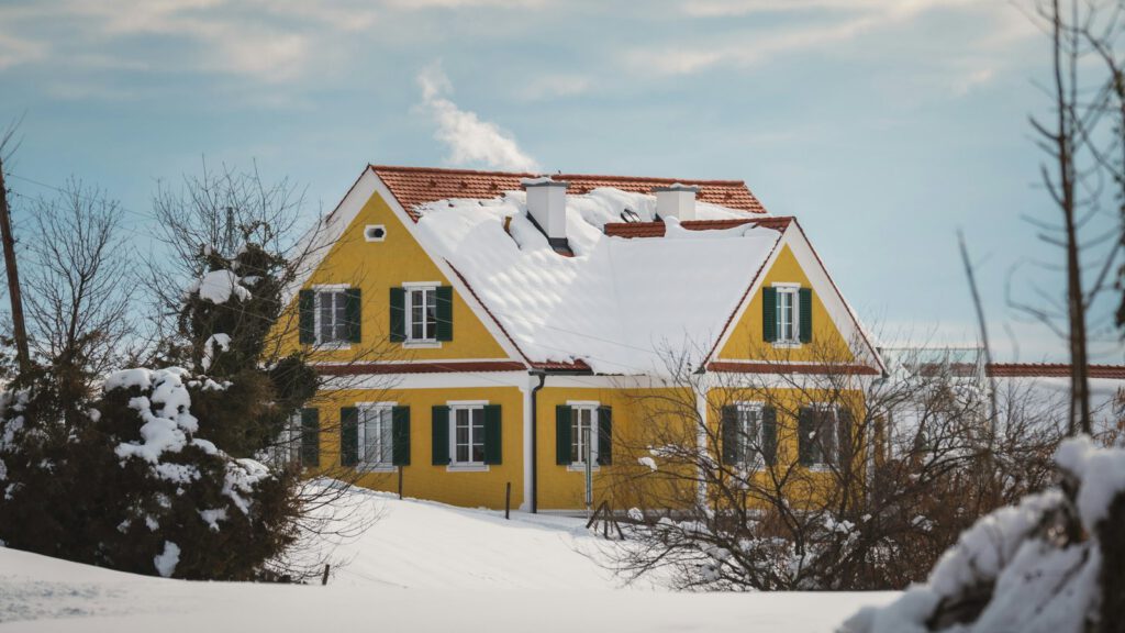 Gelbes Wohnhaus mit verschneitem Dach, aus dem Schornstein steigt eine weiße Fahne