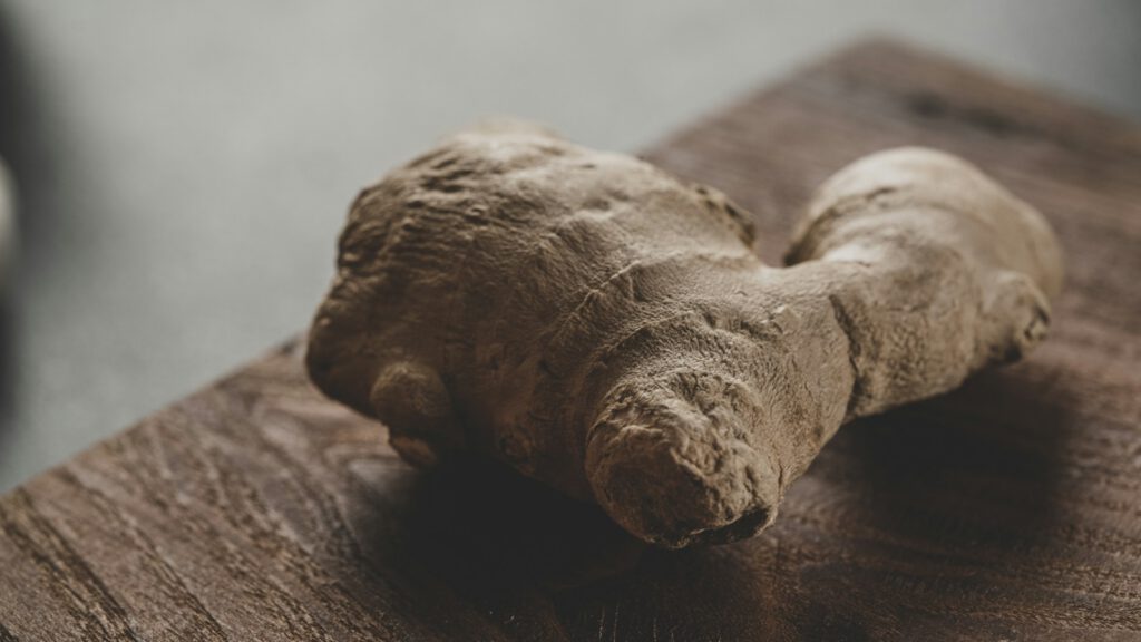 Ein ganzes Ingwer-Rhizom in Nahaufnahme auf einem dunklen Holzbrett