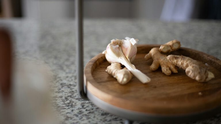 Kleine Ingwerstücke und eine Knoblauchzehe auf einem runden Holzbrett